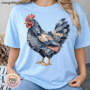 May include: Light blue t-shirt featuring a detailed denim patchwork chicken design. The chicken has a red comb and wattle, with patches of floral and checkered fabric. The shirt has short sleeves and a relaxed fit.
