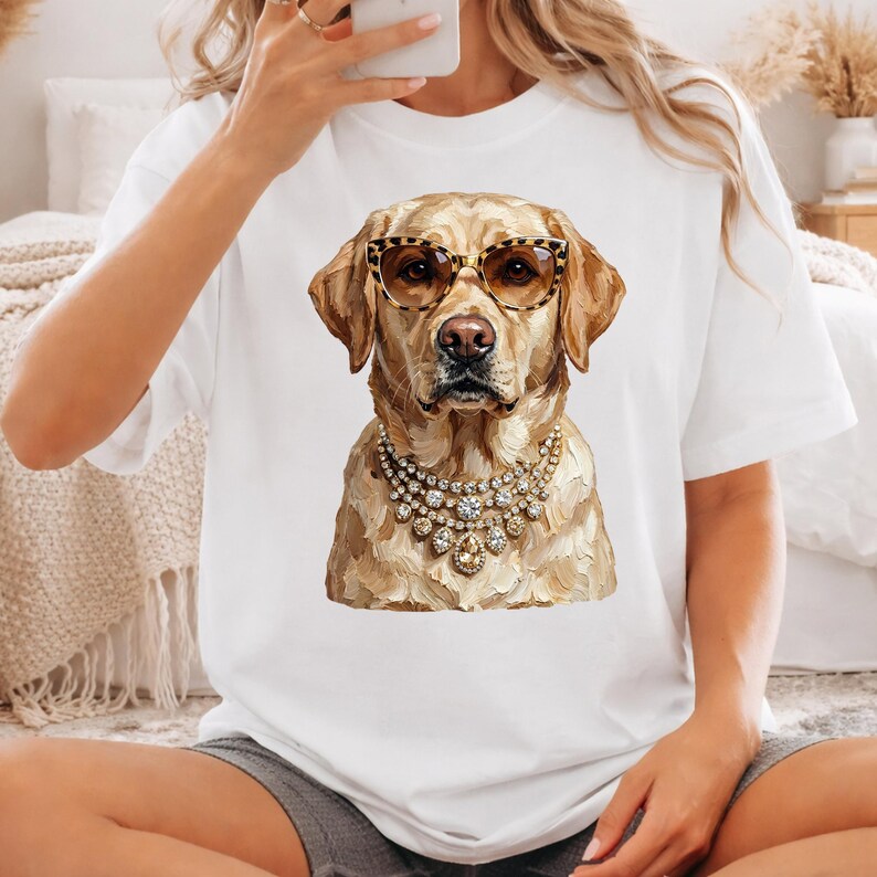 A person wearing a white t-shirt and grey shorts sits on the floor, showcasing a printed graphic of a golden retriever wearing leopard-print glasses and a crystal necklace.