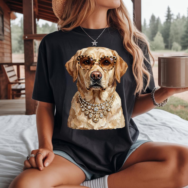 A person wearing a dark gray t-shirt featuring a graphic of a golden Labrador retriever wearing leopard-print sunglasses and a large jeweled statement necklace.