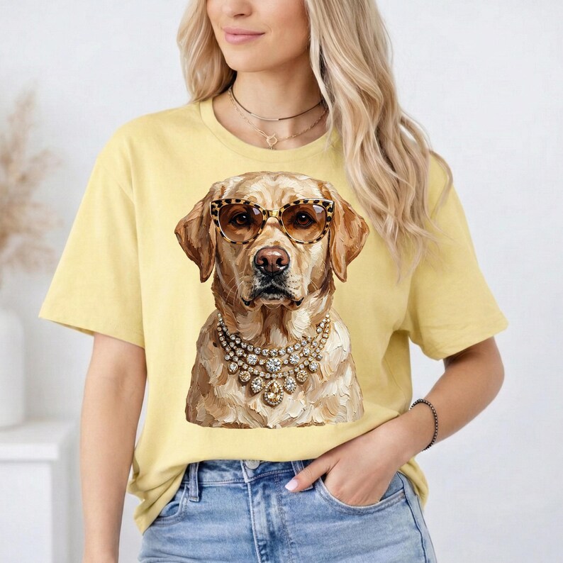 A woman wears a light yellow t-shirt printed with a golden Labrador Retriever wearing leopard-print glasses and heavy rhinestone necklaces.