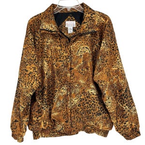 Puede incluir: Chaqueta con estampado de leopardo en tonos marrón y negro. La chaqueta tiene cuello y forro negros y está colgada de una percha blanca. Tiene un corte holgado y un dobladillo acanalado. Una prenda llamativa.