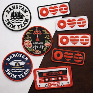May include: A collection of embroidered patches in various shapes and designs. Includes round patches with "BANGTAN SWIM TEAM" text and a ship, and a patch with a floral design and Korean text. Rectangular patches feature hearts and circles.