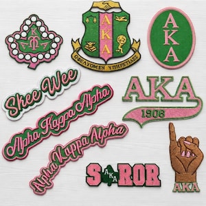 May include: A collection of embroidered patches featuring the Alpha Kappa Alpha sorority symbols, including the crest, ivy leaf, and text such as Skee Wee, Alpha Kappa Alpha, and 1906, rendered in shades of pink and green with a hand gesture icon.