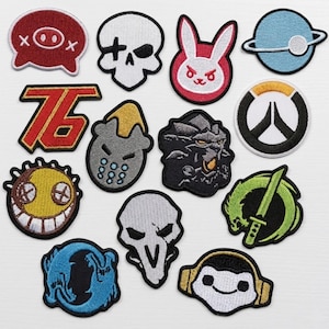 May include: A collection of embroidered patches featuring various designs. Includes a skull, a bunny, a planet, a number 76, a smiley face, a dragon, a ninja star, and other game-related symbols. Each patch has a black border.