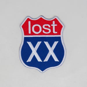 May include: A patch in the shape of a road sign with a red top section and a blue bottom section. The word "lost" is in white letters on the red section. The blue section has the white letters "XX".