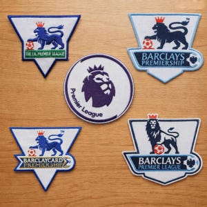 May include: Five embroidered patches featuring Premier League soccer logos. Four are shield-shaped with blue lions and soccer balls, including text for The FA Premier League, Barclays Premiership, Barclaycard Premiership, and Barclays Premier League.