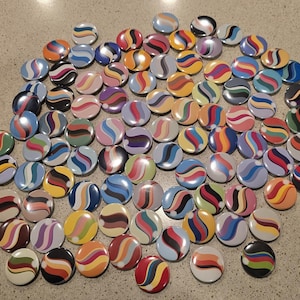 Könnte beinhalten: Eine Sammlung bunter runder Knöpfe mit einem Wirbeldesign. Die Knöpfe weisen eine Vielzahl von Farben auf, darunter Rot, Orange, Gelb, Grün, Blau, Lila und Schwarz. Die Knöpfe sind in einem verstreuten Muster angeordnet.