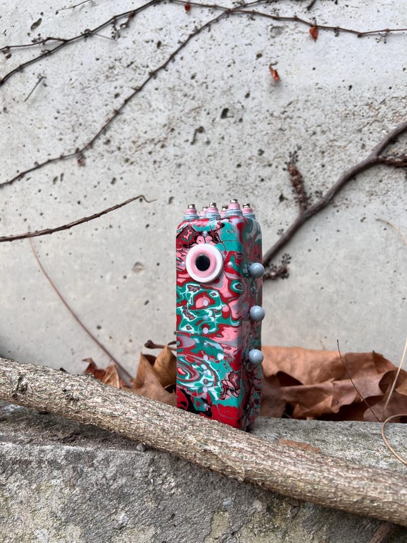 A one-of-a-kind hand-sculpted polymer clay cryptid in striking red and teal marble — the kind of weird little creature that becomes the centerpiece of any curiosity cabinet.