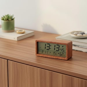 Peut inclure: Une horloge numérique en bois rectangulaire affichant l'heure, la date, la température et l'humidité. L'horloge a un cadre en bois clair et un écran numérique vert. L'heure est 13h13, la température est de 15°C.