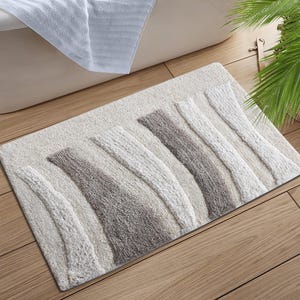 Könnte beinhalten: Ein rechteckiger Badteppich mit einem strukturierten Design in Weiß-, Grau- und Brauntönen. Der Teppich hat vertikale Streifen unterschiedlicher Breite und Textur. Der Teppich liegt auf einem Holzboden in der Nähe einer Badewanne.
