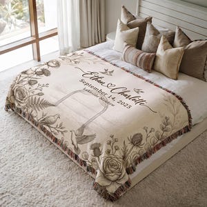 Può includere: Coperta in tessuto color crema con un design floreale e di uccelli. Presenta i nomi "Ethan & Charlotte", la data "14 settembre 2025" e "Lakeside Meadow" in elegante scrittura. La coperta ha un bordo con frange.