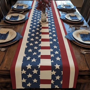 May include: A rectangular table runner with a patriotic design. The runner features a pattern of blue with white stars, red stripes, and white stripes, resembling the American flag. The runner is placed on a wooden table, with place settings visible.