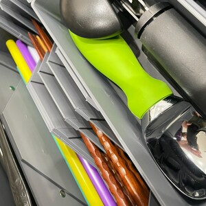 May include: A gray utensil organizer with various kitchen tools. An ice cream scoop with a green handle and a can opener are visible. Colorful chopsticks and straws in yellow, purple, and brown are also present.