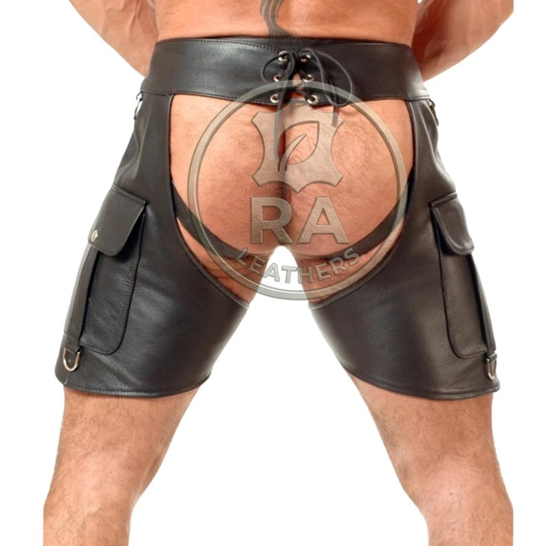 May include: Black leather chaps featuring a wide waistband with a lace-up closure at the center back. The garment includes two large cargo-style pockets on the outer thighs, each with a flap, and metal D-rings attached to the lower side seams.