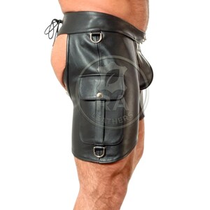 May include: Black leather shorts featuring a high-waisted design with a side-lacing closure, a prominent cargo pocket on the thigh with a snap button, and integrated metal D-rings. The garment has an open-back construction and a contoured front.