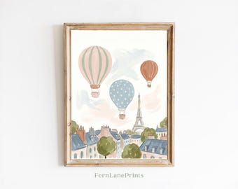 May include: A framed wall art print featuring a watercolor illustration of the Eiffel Tower and Parisian buildings under three hot air balloons in shades of pink, blue, and terracotta. The text FernLanePrints is printed at the bottom center.