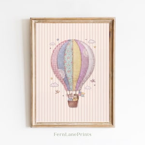 May include: A framed print featuring a whimsical hot air balloon design. The balloon is composed of patchwork fabrics in pink, blue, and yellow. The basket holds two small figures. The background is a striped pattern in soft pink. The text "FernLanePrints" is at the bottom.