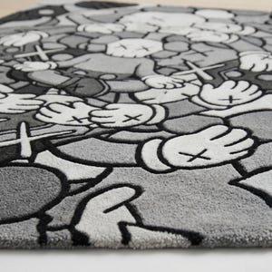 May include: A rectangular area rug featuring a repeating pattern of cartoon-style characters with X-shaped eyes and gloved hands. The design is rendered in shades of gray, white, and black, with thick black outlines defining each graphic element.
