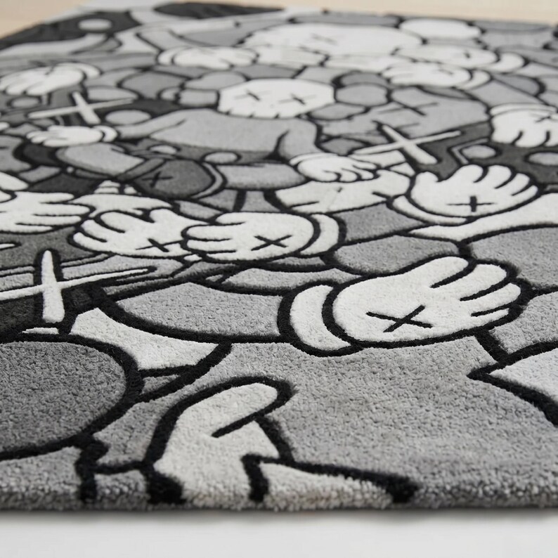 May include: A rectangular area rug featuring a repeating pattern of cartoon-style characters with X-shaped eyes and gloved hands. The design is rendered in shades of gray, white, and black, with thick black outlines defining each graphic element.