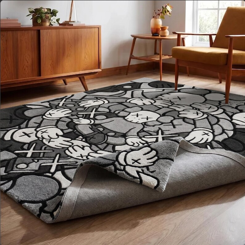 May include: A rectangular area rug featuring a repeating grayscale pattern of cartoon-style characters with X-shaped eyes and gloved hands. The rug has a thick, tufted texture with a folded corner revealing a light gray fabric backing on the underside.