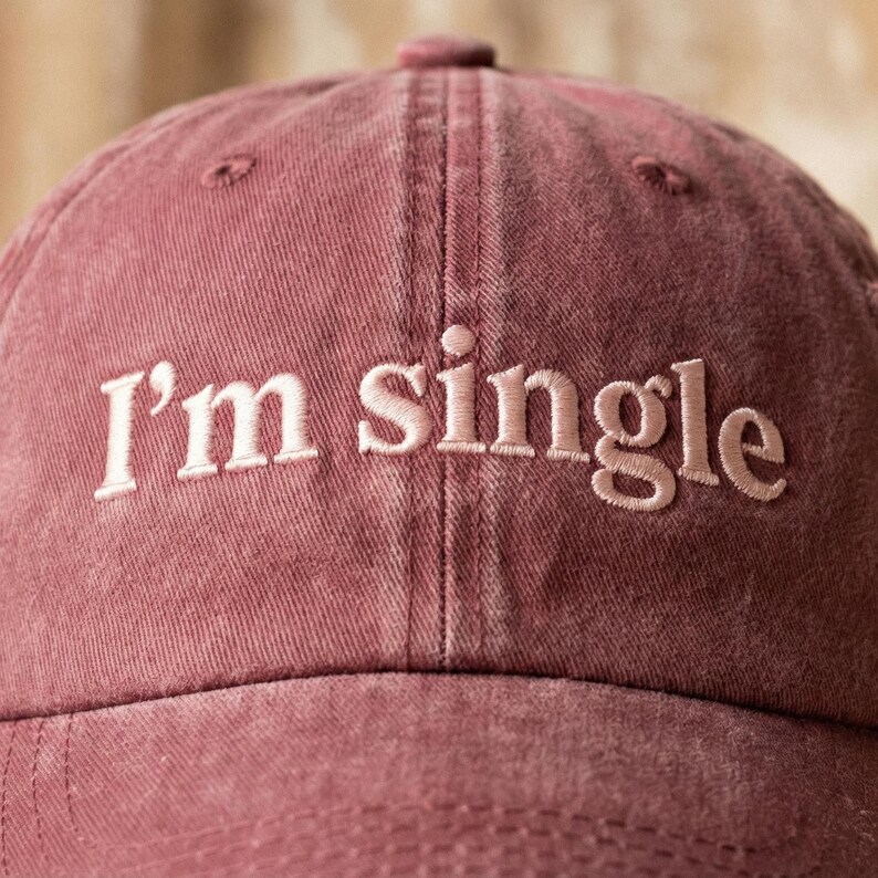 May include: A dusty rose baseball cap with the embroidered text "I'm single" in a lighter shade of pink. The cap has a curved brim and a six-panel design, perfect for casual wear.