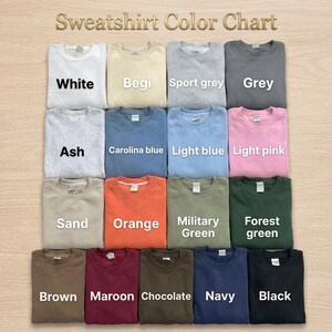 May include: A sweatshirt color chart featuring fifteen crewneck sweatshirts in various colors including white, beige, sport grey, grey, ash, carolina blue, light blue, light pink, sand, orange, military green, forest green, brown, maroon, chocolate, navy, and black.