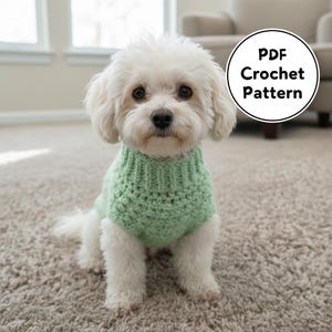 May include: A small white dog wearing a light green crocheted sweater. The dog is sitting on a carpeted floor. A circular graphic in the upper right corner reads "PDF Crochet Pattern".