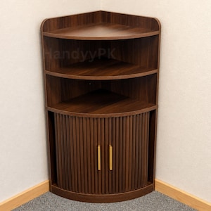 May include: A dark brown wooden corner cabinet featuring two open shelves at the top and a lower storage section with two curved, slatted doors. The doors are accented with vertical gold-toned handles. The text HandyyPK is visible on the shelf.