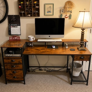 May include: An L-shaped computer desk with a rustic brown wood-grain finish and a black metal frame. It features a raised monitor shelf, three drawers on the left, one drawer on the right, a lower storage shelf, and a built-in side compartment.
