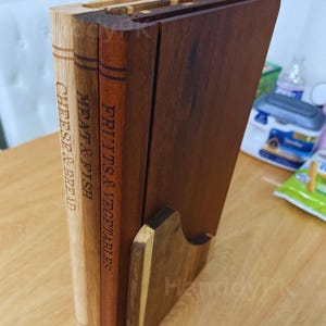 May include: A wooden cutting board set with three boards labeled "Cheese & Bread", "Meat & Fish", and "Fruits & Vegetables". The boards are in a wooden holder. The wood tones vary from light to dark brown.