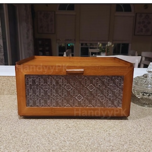 May include: A rectangular wooden box with a glass panel featuring a decorative pattern. The box has a light brown finish and a small handle on the top. The text "HandyyPK" is visible on the front.