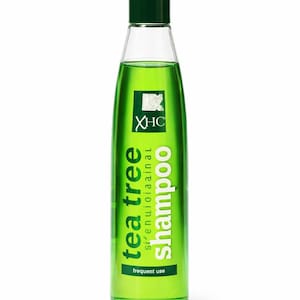 May include: A green bottle of tea tree shampoo with a dark green cap. The label features the words "tea tree shampoo" in white and green, along with the text "frequent use". The bottle contains a bright green liquid.