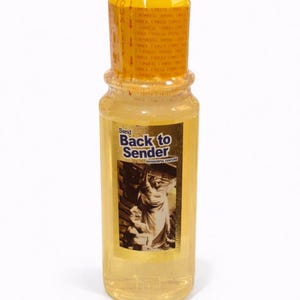 May include: A clear glass bottle with a yellow cap and a gold label. The label reads "Send Back to Sender" with an image of a statue. The bottle contains a light yellow liquid.