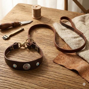 Könnte beinhalten: Ein braunes Lederhalsband für Hunde mit türkisfarbenen und silbernen Verzierungen und eine passende Leine liegen auf einer Holzoberfläche. Werkzeuge und eine Garnrolle sind ebenfalls zu sehen, was auf ein handgefertigtes Produkt hindeutet.