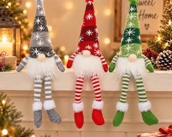 May include: Three plush gnome figurines with long dangling legs, wearing tall knit hats in gray, red, and green with white snowflake patterns and star toppers. Each gnome features a round nose, a white faux fur beard, and striped legs.