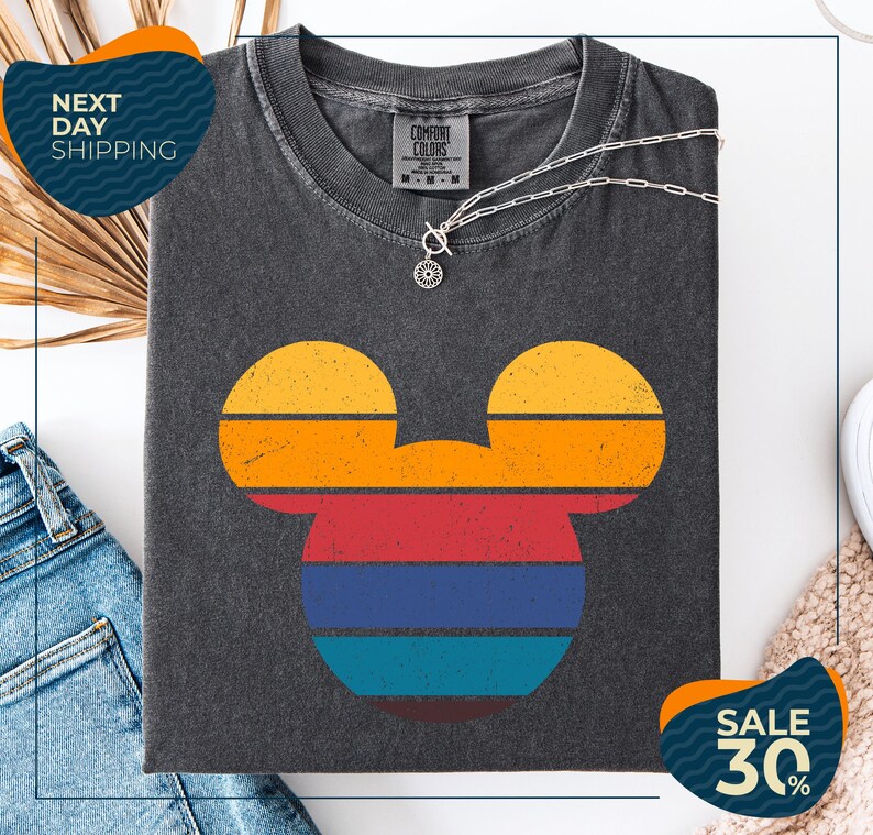 a gray t-shirt with a colorful Mickey Mouse design, along with a pair of jeans and a beige sweater. The t-shirt is displayed on a white background, and there are two sale signs indicating a 30% discount.