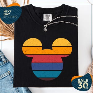 a black t-shirt with a colorful Mickey Mouse design, along with a pair of jeans and a necklace. The t-shirt is displayed on a white background, and there are two sale signs indicating a 30% discount.