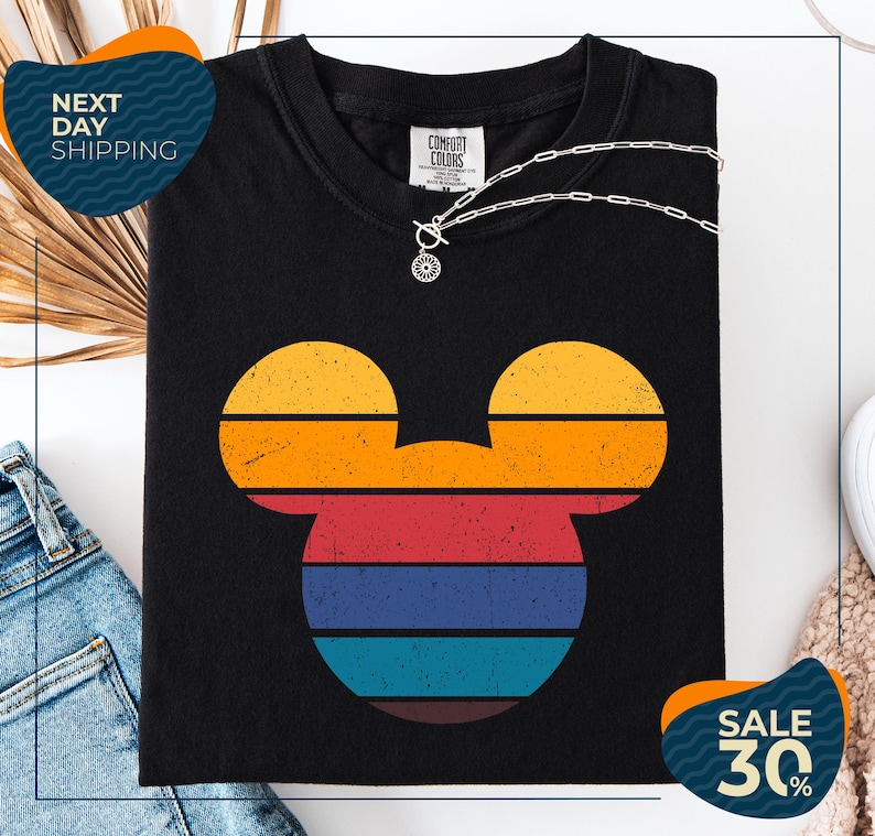 a black t-shirt with a colorful Mickey Mouse design, along with a pair of jeans and a necklace. The t-shirt is displayed on a white background, and there are two sale signs indicating a 30% discount.