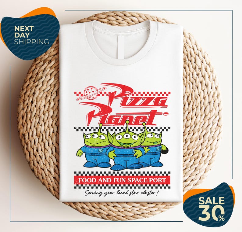 A white t-shirt with a graphic design featuring three alien characters from the Pixar movie "Pizza Planet" and the text "Food and Fun Space Port" along with a sale offer.