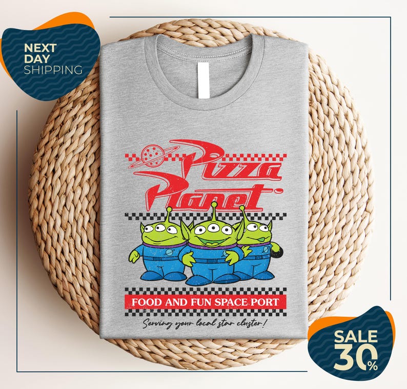 a gray t-shirt with a graphic design of three alien characters from the Pixar movie "Pizza Planet" and text promoting a food and fun space port.