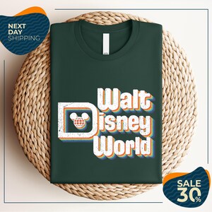 A green t-shirt with the text "Walt Disney World" printed on it, placed on a woven basket.