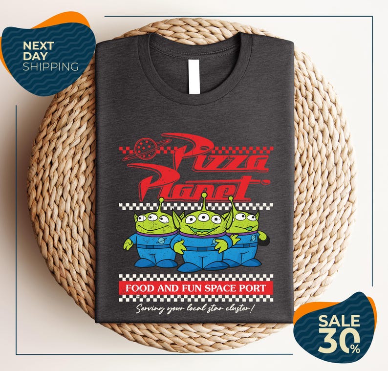 a gray t-shirt with a graphic design of three alien characters from the Pixar movie "Pizza Planet" and text promoting a food and fun space port.