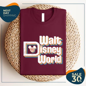A burgundy t-shirt with the text "Walt Disney World" printed on it, displayed on a woven basket.