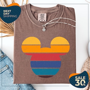 a brown t-shirt with a colorful Mickey Mouse design, along with a denim jacket and a necklace. The t-shirt is displayed on a white background, and there are two sale signs indicating a 30% discount.