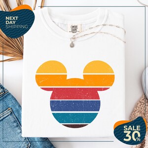 a white t-shirt with a colorful Mickey Mouse design, along with a pair of jeans and a necklace. The t-shirt is displayed on a white background, and there are two sale signs indicating a 30% discount.