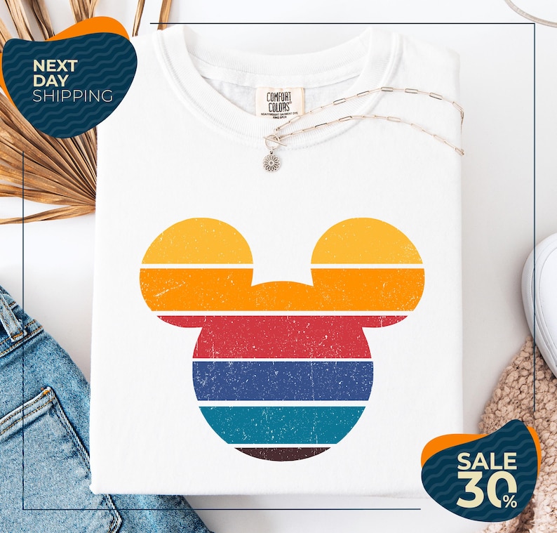 a white t-shirt with a colorful Mickey Mouse design, along with a pair of jeans and a necklace. The t-shirt is displayed on a white background, and there are two sale signs indicating a 30% discount.