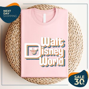A pink t-shirt with the text "Walt Disney World" printed on it, placed on a woven basket.