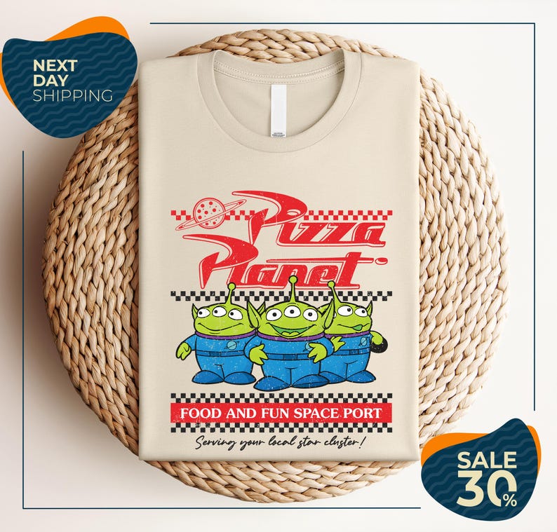 a t-shirt with a design related to the popular animated movie "Pizza Planet". The t-shirt is displayed on a woven basket, and there are two sale signs in the image.