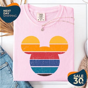 a pink t-shirt with a colorful Mickey Mouse design, along with a pair of jeans and a necklace. The t-shirt is displayed on a white background, and there are two sale signs indicating a 30% discount.
