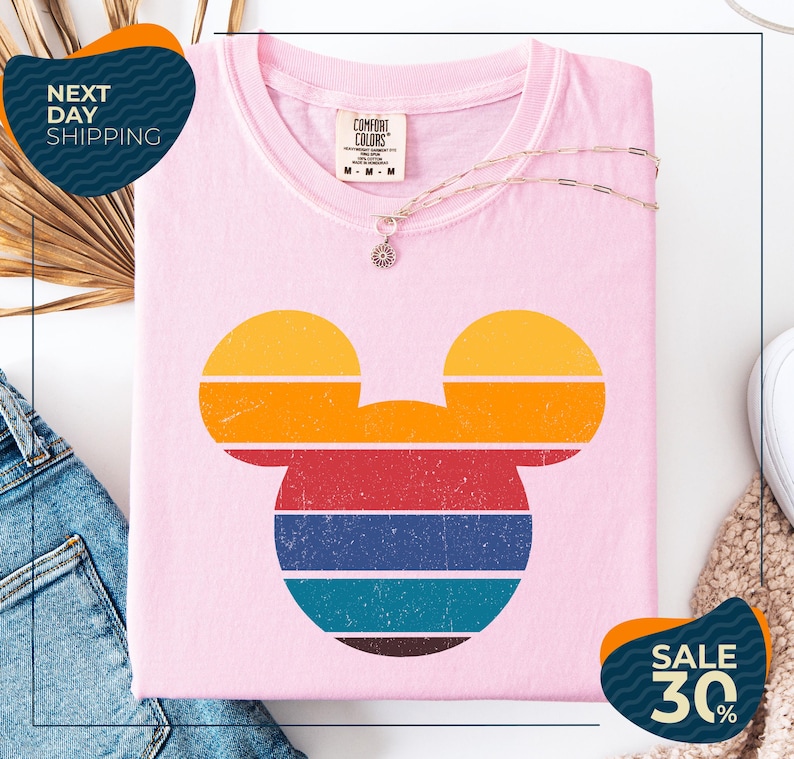 a pink t-shirt with a colorful Mickey Mouse design, along with a pair of jeans and a necklace. The t-shirt is displayed on a white background, and there are two sale signs indicating a 30% discount.